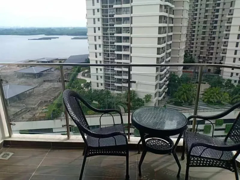 Balcony features: glass railing, two black wicker chairs, round glass-top table, tiled flooring, view of water, view of surrounding buildings, greenery in the distance; style: modern; view: water.