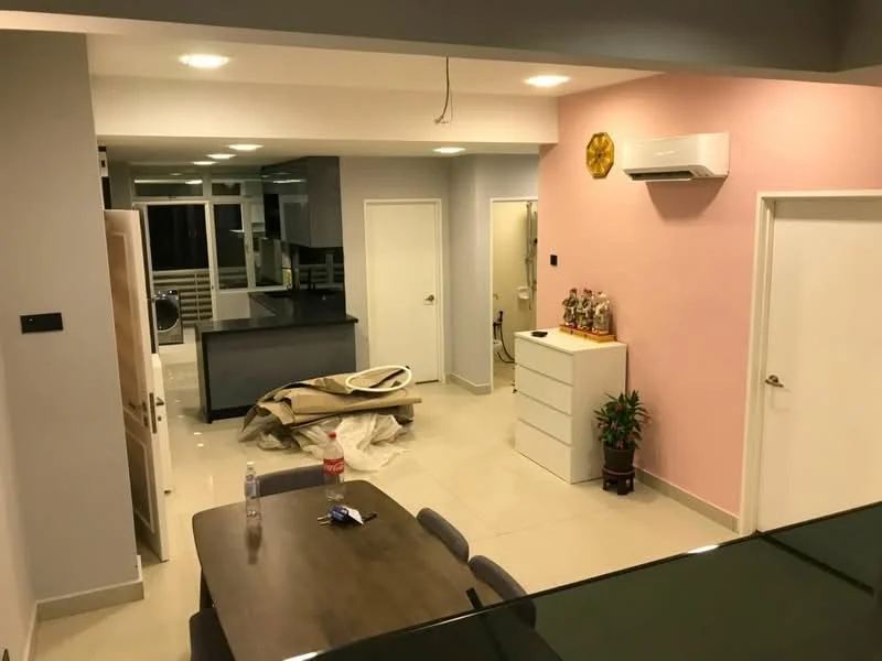 Living features: light grey painted walls, pink accent wall, white ceiling, recessed downlights, wall-mounted split AC, dining table, chairs, floor tiles, large windows, open layout, decorative plant, white dresser, kitchen island with black countertop, unmade sofa with covering; style: modern.