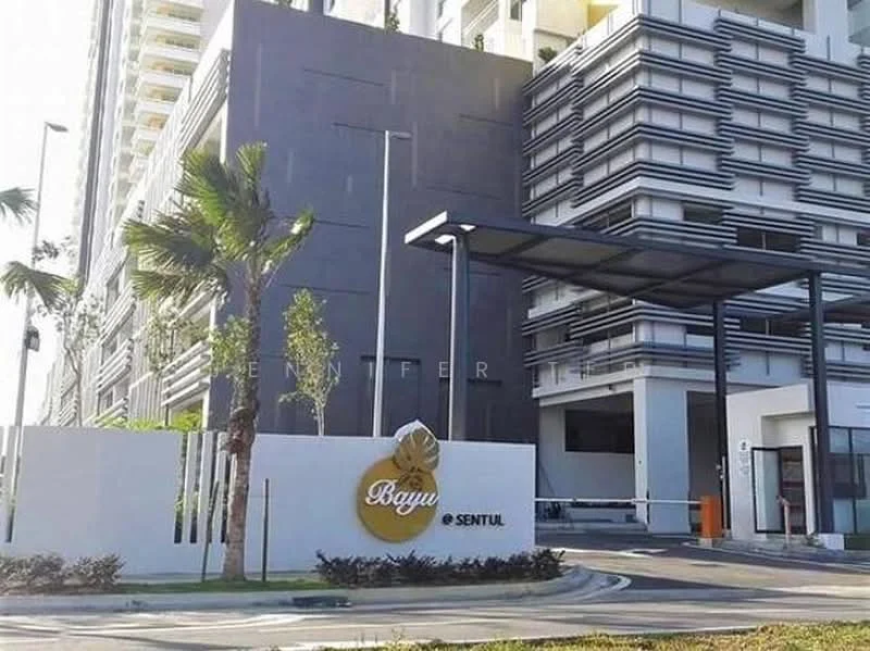 Exterior type: high-rise condominium; features: modern facade with grey and white cladding, prominent entrance sign with logo, covered entrance with awning, landscaped garden with palm trees, driveway with interlocking pavers, security gate at entrance, surrounded by greenery; style: modern.