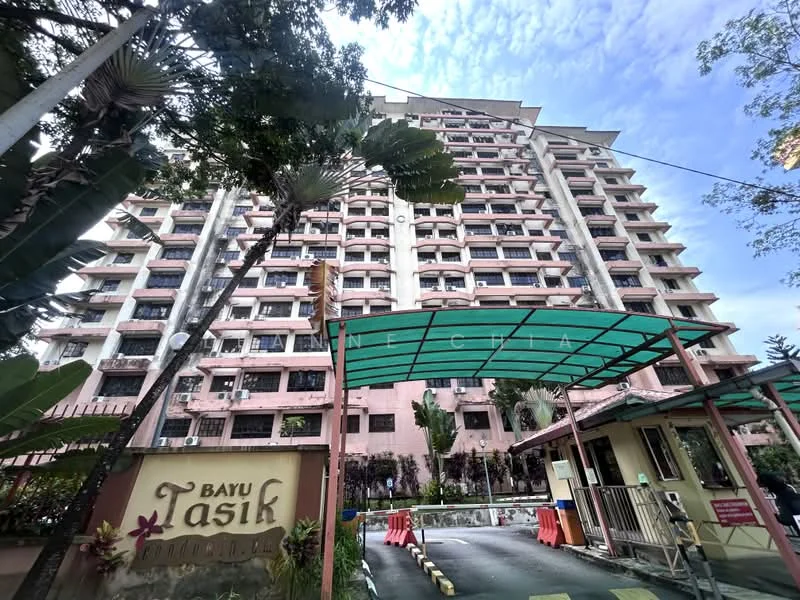 Exterior type: mid-rise condominium; features: pink painted facade, glass curtain wall, recessed balconies, security guard house at entrance, covered parking, manicured landscaping, palm trees, signage with 'Bayu Tasik', multiple storeys, visible air conditioning units; style: modern.