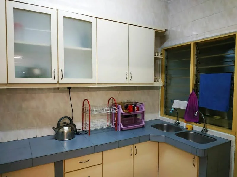 Kitchen features: light wood cabinetry with glass-front upper cabinets, grey countertop, double-bowl stainless-steel sink, chrome faucet, kettle, dish rack, colorful storage rack, window with louvered glass, purple towel, blue towel.