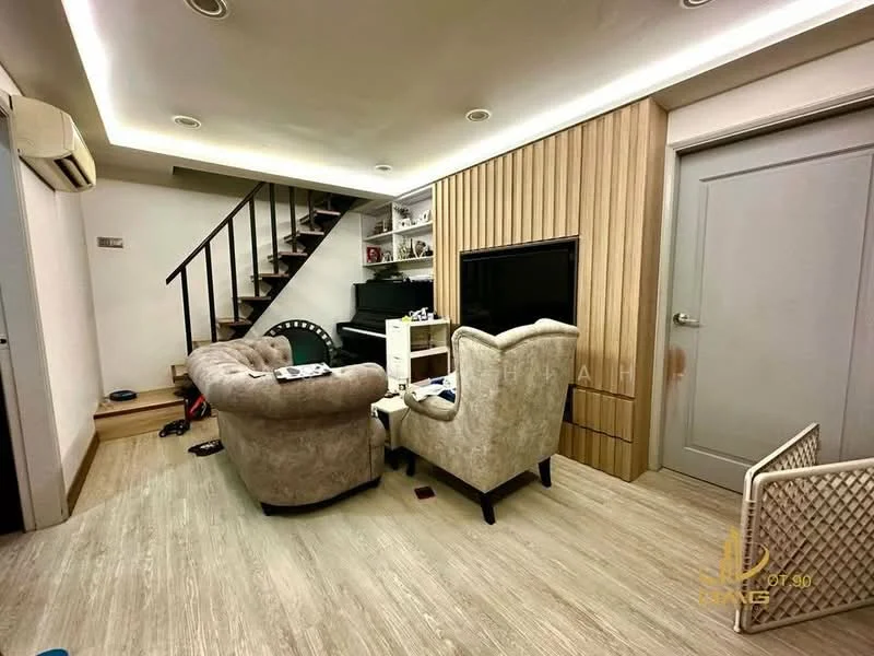 Living features: light wood flooring, white painted walls, wood panel accent wall, sofa with beige upholstery, armchair with beige upholstery, TV console, wall-mounted TV, staircase with wooden steps, open shelving, recessed ceiling lights, air conditioning unit; style: modern.