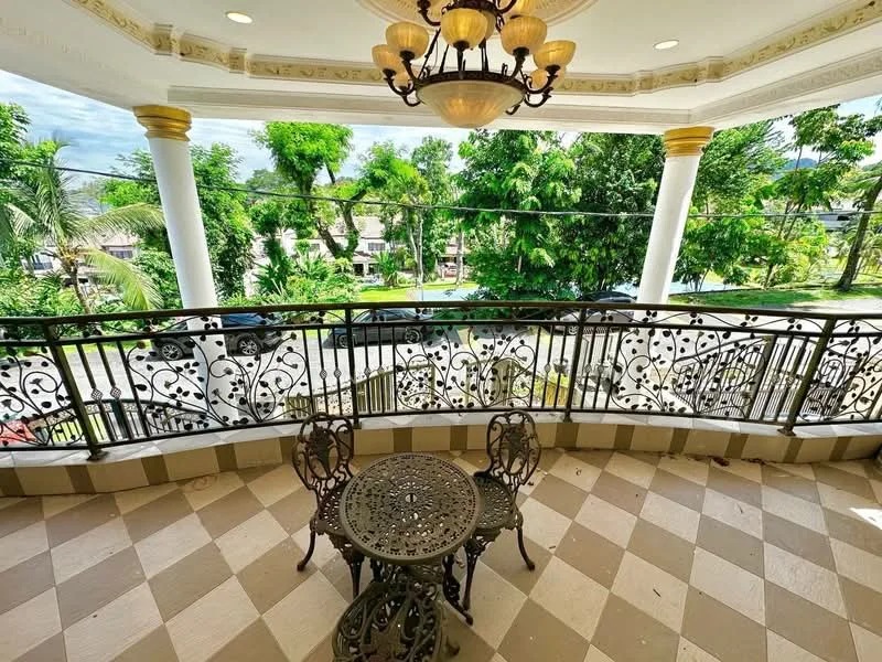 Balcony features: decorative wrought iron railing, checkered patterned flooring, round metal table, two metal chairs, chandelier with multiple bulbs, ceiling with decorative moulding, outdoor view of greenery, outdoor view of street; style: luxury; view: garden.