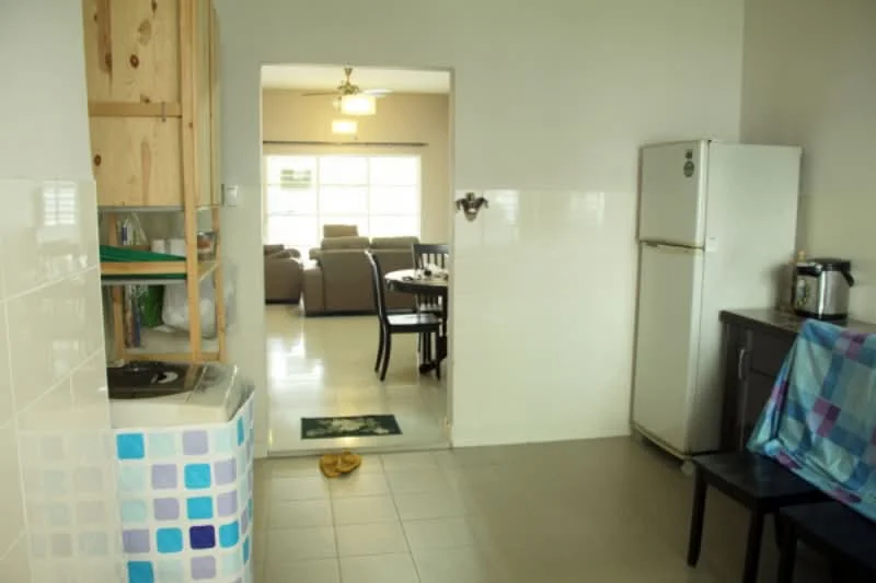 Kitchen features: white tiled walls, light grey tiled flooring, wooden cabinetry, stainless-steel fridge, built-in stove, black countertop, kitchen sink, open layout to living area; style: modern. Living features: sofa set, dining table, light fixture, large windows, carpeted area, decorative rug; style: modern.