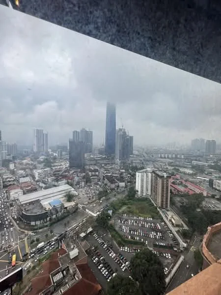 Exterior type: high-rise condominium; features: city skyline view, surrounded by urban landscape, visible traffic on roads, multiple high-rise buildings, open-air parking lot, cloudy sky, distant landmark tower, mixed-use development in foreground; style: modern.