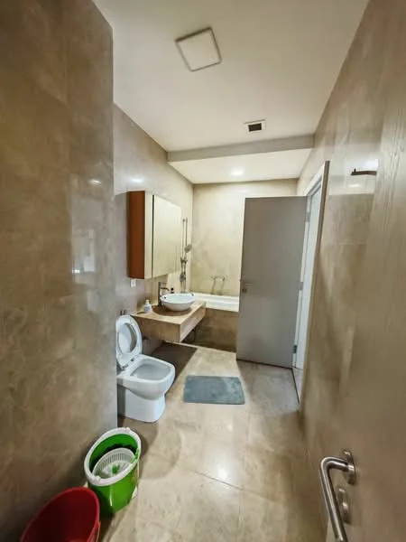 Bathroom features: cream marble tile flooring, cream tiled walls, single-sink vanity with wood cabinet, chrome basin mixer faucet, framed mirror above vanity, one-piece toilet, shower area with glass partition, recessed downlights, towel rail, grey bath mat, green waste bin, green laundry basket; style: modern.