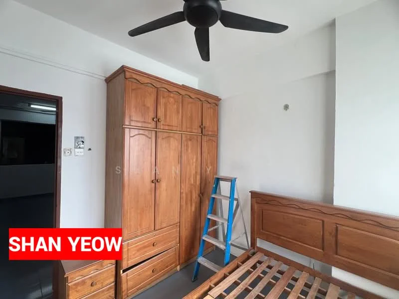 Bedroom features: wooden wardrobe with multiple compartments, wooden bed frame without mattress, ceiling fan, white painted walls, grey tiled flooring, ladder, window with no visible treatment.
