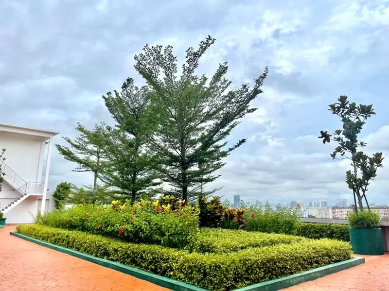 Exterior type: landscape garden; features: manicured lawn, mature trees, flowering plants, green hedges, paved walkway, urban skyline in background; style: modern.