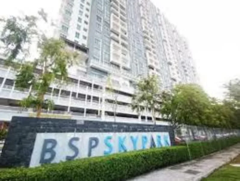 Exterior type: high-rise condominium; features: grey facade with balconies, landscaped garden with hedges, manicured lawn, multi-storey car park, signage with 'BSP Skypark', surrounded by trees; style: modern.