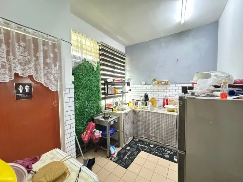 Kitchen features: white tiled walls, grey painted wall, ceramic tile flooring, stainless-steel sink, chrome faucet, kitchen cabinets with checkered pattern, countertop with checkered pattern, refrigerator, various kitchen utensils, decorative green wall panel, window with horizontal blinds, area rug with coffee print. Room features: toilet door with signage.
