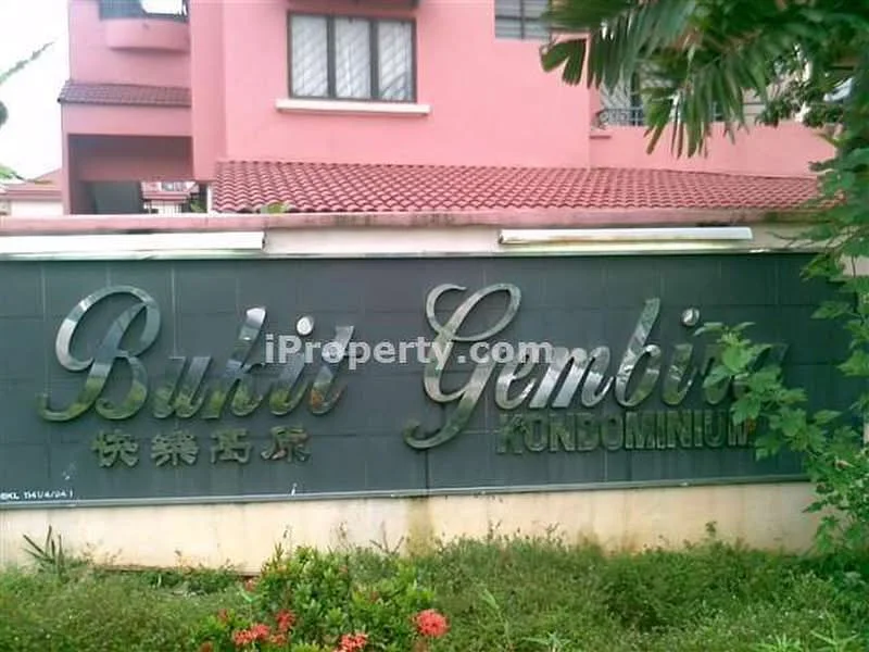 Exterior type: low-rise condominium; features: signage with name 'Bukit Gembira', green landscaping, manicured garden, brick wall, red tiled roof, multiple windows visible, surrounding greenery; style: modern.
