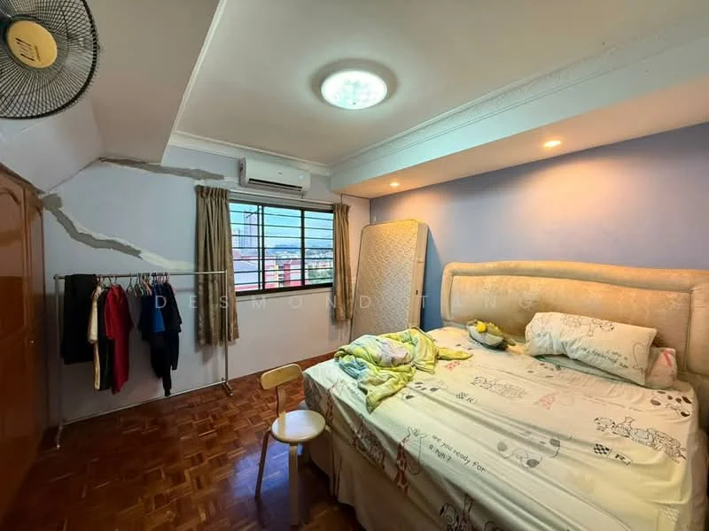 Bedroom features: wooden flooring, blue painted walls, white ceiling with crown moulding, 5-blade ceiling fan, floor-to-ceiling window, curtains, double bed with upholstered headboard, bedding with cartoon pattern, wooden wardrobe, clothes hanging on hooks, small wooden chair; view: city.