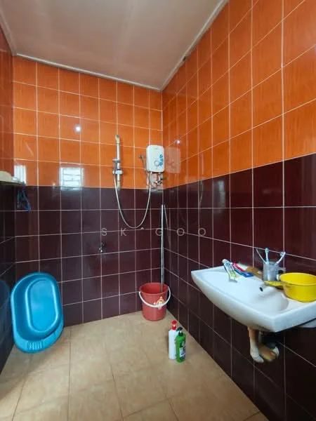 Bathroom features: orange tiled walls, brown tiled walls, ceramic tile flooring, wall-mounted shower with adjustable head, sink with wall-mounted faucet, blue plastic bathtub, red plastic bucket, cleaning supplies on the floor.