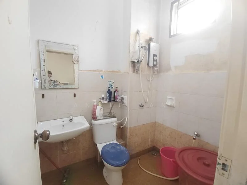 Bathroom features: white tiled walls, beige tiled flooring, single-sink vanity with mirror, toilet, shower with handheld shower head, water heater, plastic bucket, wall-mounted soap dispenser.