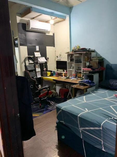 Bedroom features: blue painted walls, wooden flooring, queen-size bed with blue bedding, desk with computer monitor, office chair, shelves with various items, cluttered workspace, air conditioning unit, overhead lighting, window with no visible treatment.