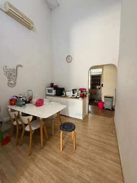 Kitchen features: white walls, wooden flooring, high ceiling, dining table with 4 chairs, stool, microwave, kettle, toaster, electric rice cooker, dishwasher, sink, wall-mounted air conditioning unit, clock on wall, open archway to another room, pink trash bin; style: modern.