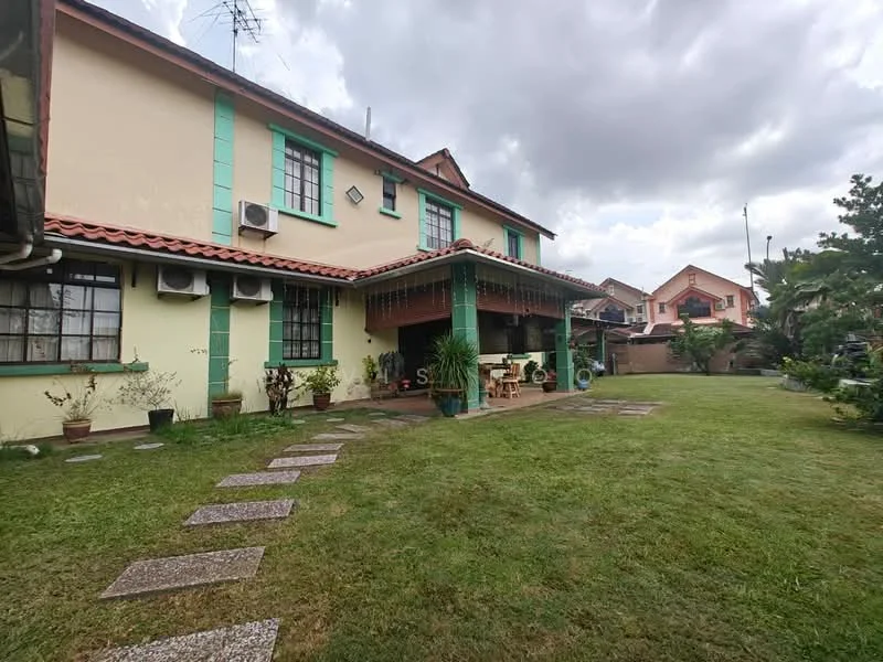 Exterior type: detached bungalow; features: green painted facade, red tiled roof, single-storey, manicured lawn, stone-paved walkway, outdoor dining area with table and chairs, air conditioning units visible on facade, surrounded by greenery, garden plants in pots, covered porch area; style: traditional.