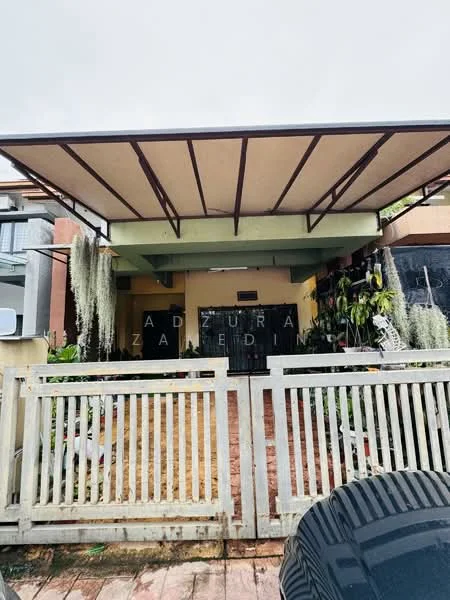 Exterior type: detached bungalow; features: flat roof with overhang, green painted facade, wooden front door, white picket fence, landscaped garden with plants, stone pathway, exterior wall with decorative elements, visible parking area; style: modern.