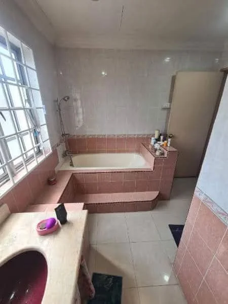 Bathroom features: bathtub, showerhead, pink tiled walls, white bathtub, sink with countertop, mirror, window with grid design, floor tiles, toilet, step-up platform, storage products on countertop.
