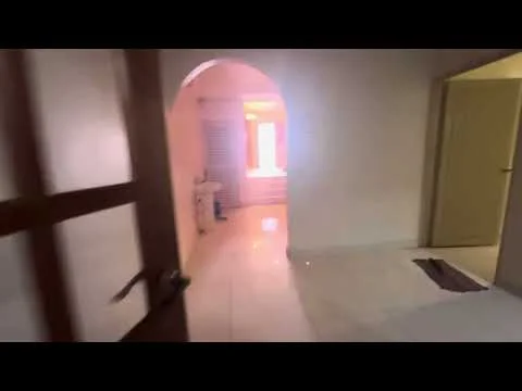 Room features: white painted walls, glossy tile flooring, arched doorway, natural light from window, door leading to another room, neutral color scheme, minimalist decor; style: modern.