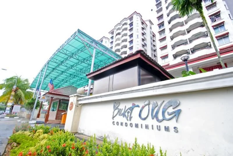 Exterior type: high-rise condominium; features: glass canopy entrance, white painted facade, multiple storeys, landscaped garden with flowers, security guardhouse, paved walkway, flag poles, street lighting, surrounded by greenery; style: modern.