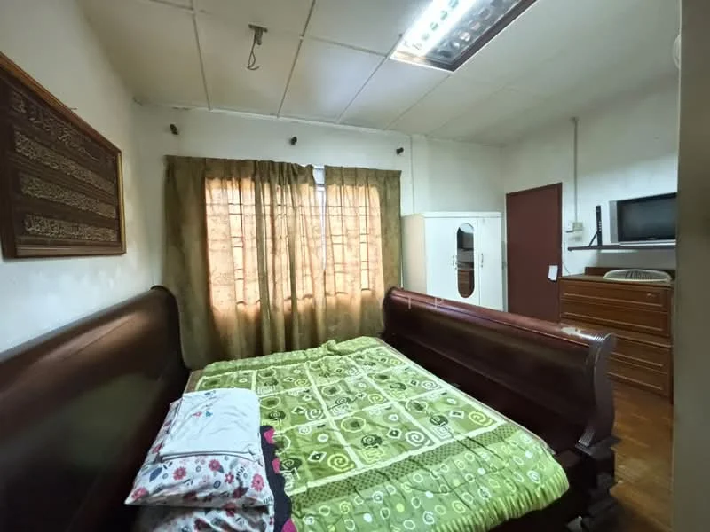 Bedroom features: queen-size bed with wooden frame, green patterned bedspread, two decorative pillows, wooden dresser, wall-mounted TV, curtains in brown, wooden wall art, flooring in polished wood, ceiling light fixture, mirror on the wall.