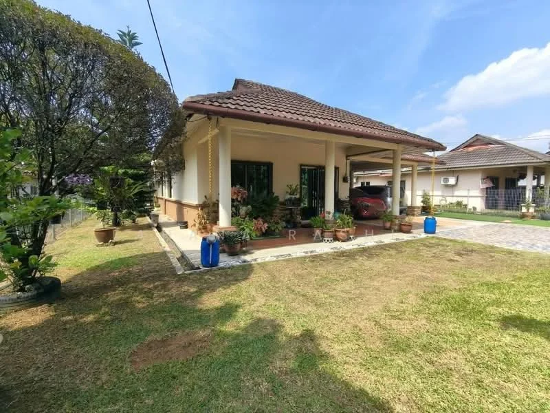 Exterior type: detached bungalow; features: single-storey, pitched tile roof, cream painted facade, manicured lawn, landscaped garden with potted plants, driveway with interlocking pavers, covered porch, windows with black frames, visible car parked, surrounded by mature trees; style: traditional.