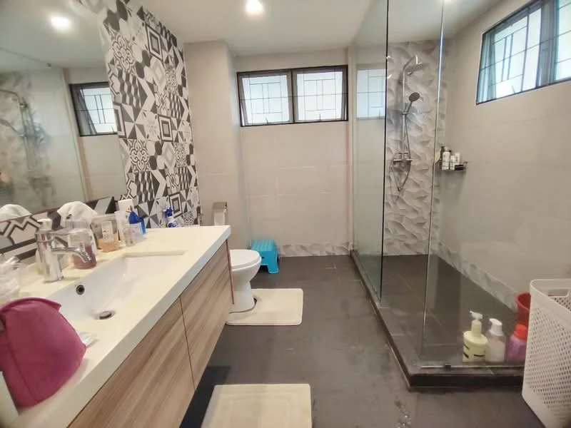 Bathroom features: single-sink vanity with wood cabinet, chrome basin mixer faucet, framed mirror, one-piece toilet, walk-in shower with glass enclosure, rain shower head, tile cladding on walls, dark tile flooring, white bath mat, shower caddy, various toiletries on vanity, blue stool; style: modern.