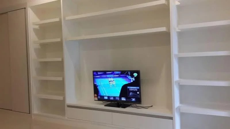 Living features: built-in white shelving units, flat-screen TV, white cabinetry below TV, light-colored flooring, neutral wall color, minimalist design, open space layout, no visible decor; style: modern.