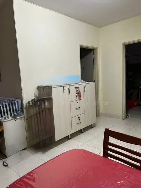 Room features: light-colored painted walls, white tiled flooring, wooden dining table, red tablecloth on dining table, cupboard with drawers, open doorway leading to another room, visible kitchen appliances in background.