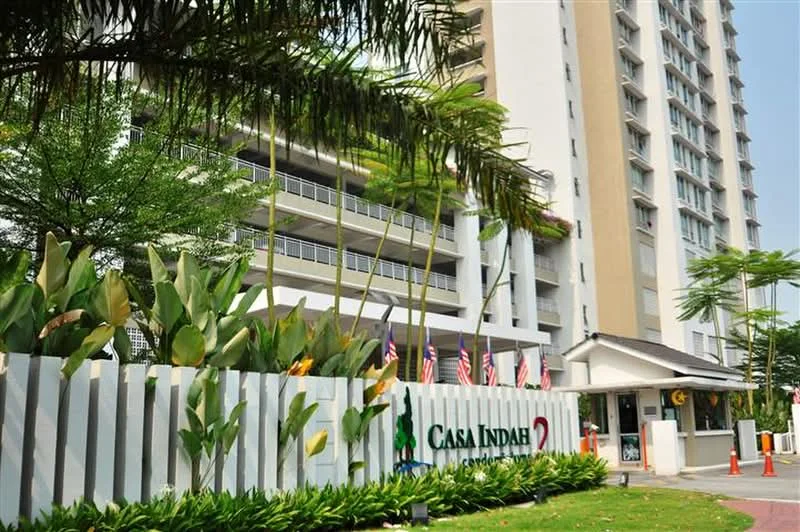 Exterior type: high-rise condominium; features: white painted facade, green landscaping with palm trees, manicured lawn, covered parking area, security guard house at entrance, multiple floors visible, balconies on upper floors, flags displayed at entrance; style: modern.