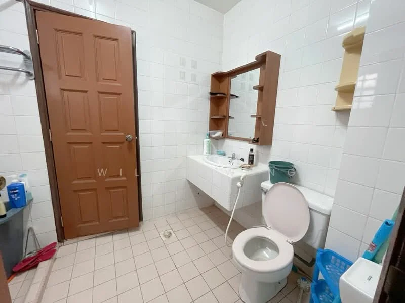 Bathroom features: white tiled walls, light grey tiled flooring, single-sink vanity with mirror, toilet, shower hose, shelves above sink, storage cabinet, door, waste bin.