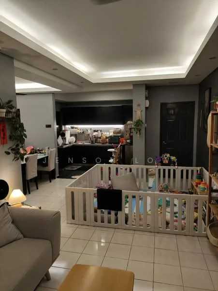 Living features: cream painted walls, white ceiling with recessed lighting, tile flooring, 3-seater fabric sofa in light grey, wooden coffee table, decorative plants, playpen with colorful toys, floor lamp, open layout to kitchen, dining area visible in background; style: modern. Kitchen features: black cabinetry, stainless-steel appliances, kitchen island, countertop with bar stools, under-cabinet lighting, open shelving, microwave, sink, cooking utensils visible; style: modern.