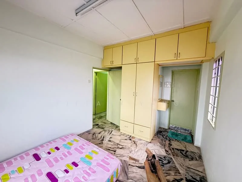 Bedroom features: queen-size bed with pink patterned bedding, built-in wardrobe with yellow cabinetry, marble flooring, white painted walls, ceiling light fixture, window with metal grille, green door leading to another room, small wall-mounted shelf.
