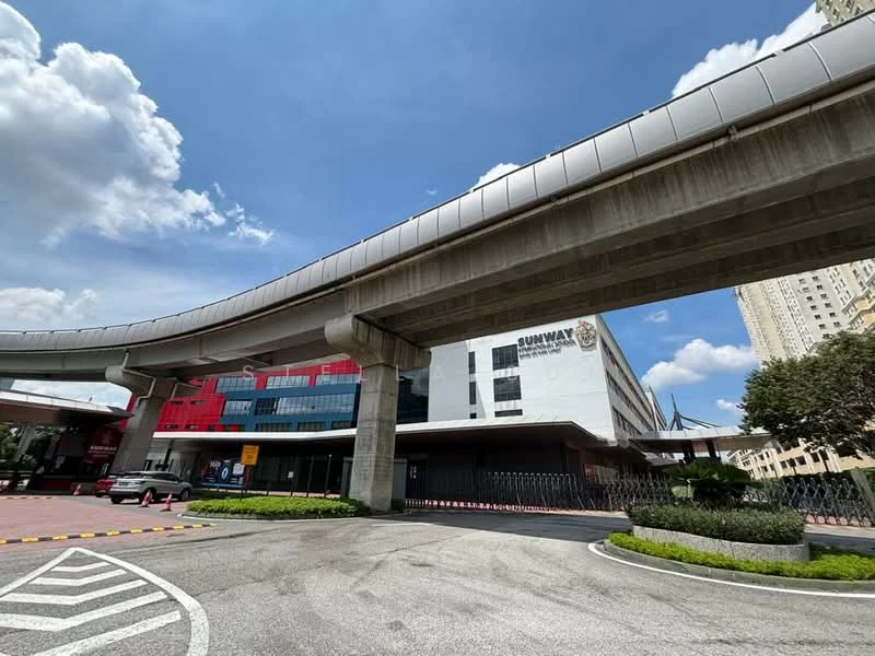 Exterior type: commercial building; features: modern facade with glass and concrete, overhead monorail track, paved driveway, landscaped garden with shrubs, parking area, entrance with security gate, signage for Sunway, surrounding high-rise buildings, clear blue sky; style: modern.