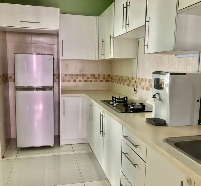 Kitchen features: white cabinetry, stainless-steel fridge, gas stove with 2 burners, white countertop, tile backsplash with beige and brown pattern, sink with chrome faucet, white tiled flooring, green accent wall; style: modern.