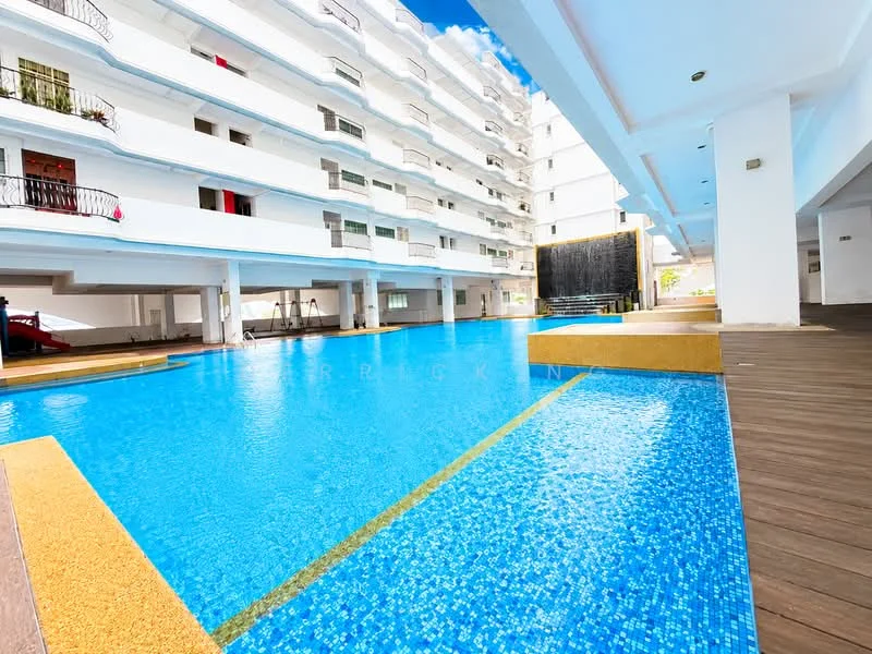 Exterior type: mid-rise condominium; features: swimming pool, pool deck with loungers, water feature wall, white painted facade, balconies with black railings, landscaped area, wooden decking, sunny outdoor space; style: modern.