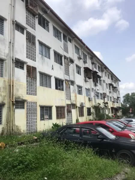 Exterior type: low-rise apartment block; features: white painted facade, grilled windows, exposed concrete, multiple air conditioning units, ground-level parking area, overgrown grass, nearby trees, two-storey building, visible balconies; style: traditional.