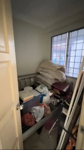 Room features: light-colored painted walls, window with grid pattern, metal shelving unit, stacked pillows, various bags and boxes, cluttered storage space, door with knob, flooring not visible.