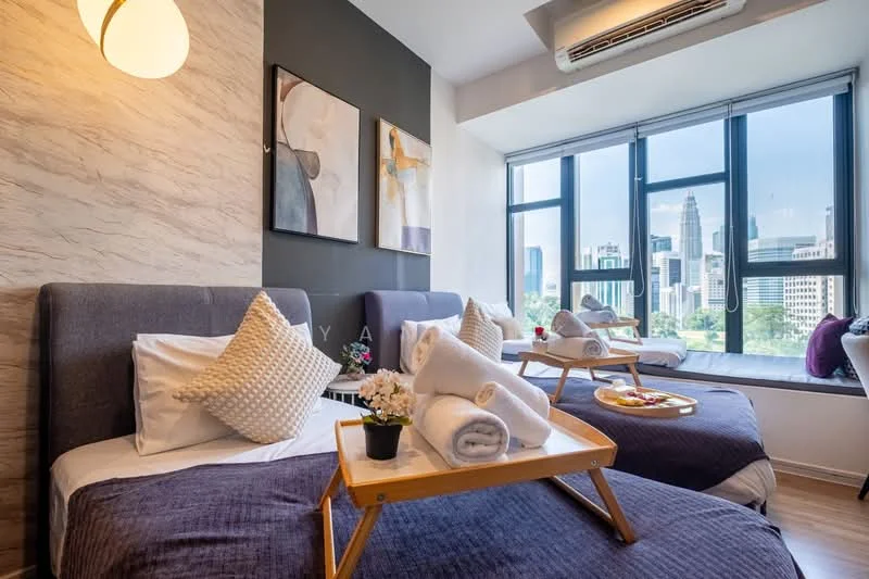 Bedroom features: two single beds with grey upholstered headboards, white bedding with decorative pillows, blue throw blankets, wooden bed trays with snacks and drinks, large windows with city view, floor-to-ceiling windows, roller blinds, wall-mounted air conditioning unit, decorative wall art, light fixture on wall, laminate flooring, small potted plant on bed tray; style: modern; view: city.