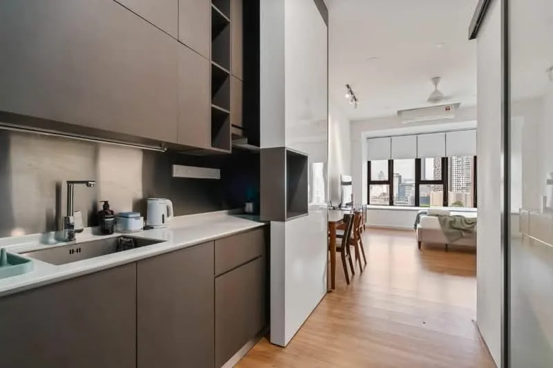 Kitchen features: dark wood cabinetry, white countertop, single-bowl stainless-steel sink, chrome pull-down faucet, built-in oven, stainless-steel kettle, stainless-steel microwave, open shelving, recessed downlights, wooden flooring, floor-to-ceiling windows, dining table with chairs visible in background; style: modern; view: city.