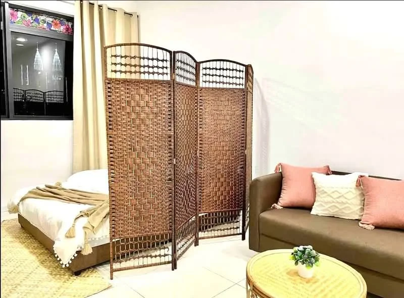 Room features: woven room divider, brown fabric sofa, pink decorative cushions, white bedding, woven area rug, light-colored tiled flooring, curtains, small round coffee table, indoor plant on table, wall with light-colored paint; style: modern.