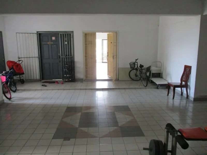 Room features: tiled flooring, white painted walls, two doors leading to other rooms, metal security grills on doors, bicycle storage, children's tricycle, wooden chair, exercise equipment, decorative tile pattern on floor.
