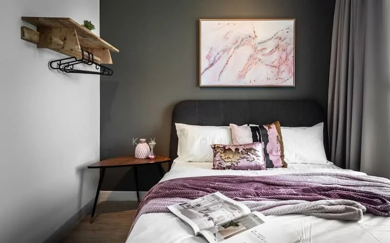 Bedroom features: queen-size bed with grey upholstered headboard, white bedding with decorative pillows, wooden side table, framed artwork with pink and white tones, wall-mounted wooden shelf, grey painted walls, light grey curtains, decorative items on shelf, magazine on bed, textured throw blanket; style: modern.