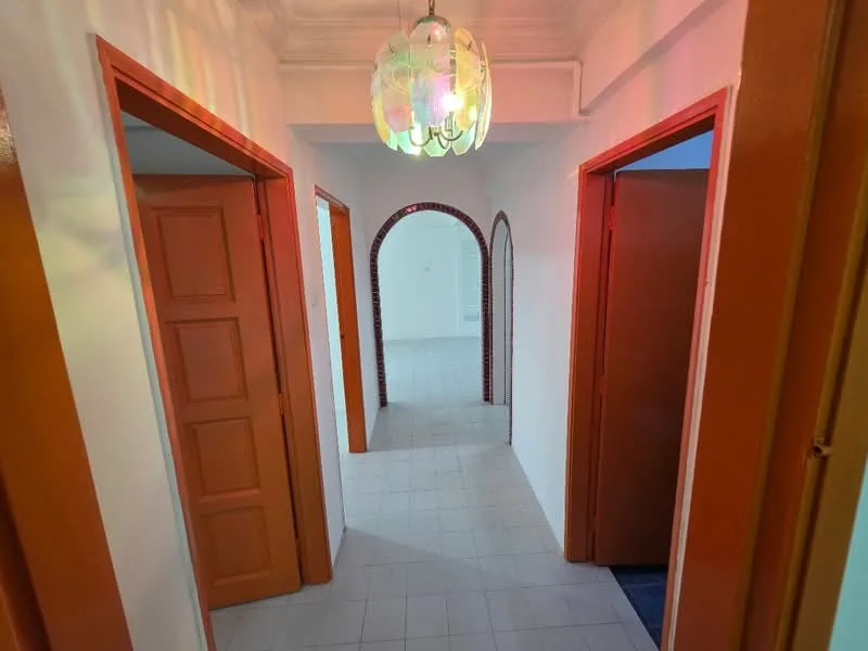 Hallway features: white painted walls, tiled flooring, arched doorway, 3 doors leading to rooms, ceiling light fixture with colorful glass, crown moulding, neutral color scheme; style: traditional.