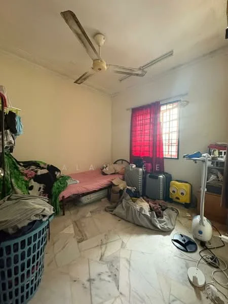 Bedroom features: single bed with pink bedding, ceiling fan, red curtains, marble flooring, clothes on bed, laundry basket, suitcases, wooden cabinet, decorative items on cabinet.