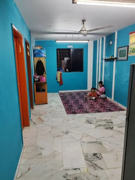 Room features: blue painted walls, white ceiling, marble flooring, area rug with geometric pattern, ceiling fan, window with black grille, shelving unit on wall, orange door, storage cabinet, two children sitting on the floor; style: modern.