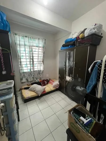 Room features: single bed with mattress and bedding, black wardrobe with glass doors, white tiled flooring, window with sheer curtains, standing fan, plastic storage boxes, wooden chair, stacked items on top of wardrobe.