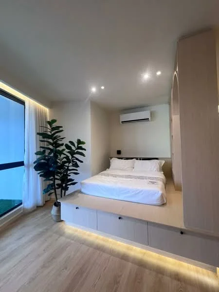 Bedroom features: king-size bed with white bedding, wooden platform bed frame, built-in bedside table with storage, recessed LED lighting, wall-mounted air conditioning unit, floor-to-ceiling windows, sheer curtains, laminate flooring, decorative indoor plant in pot; style: modern; view: garden.