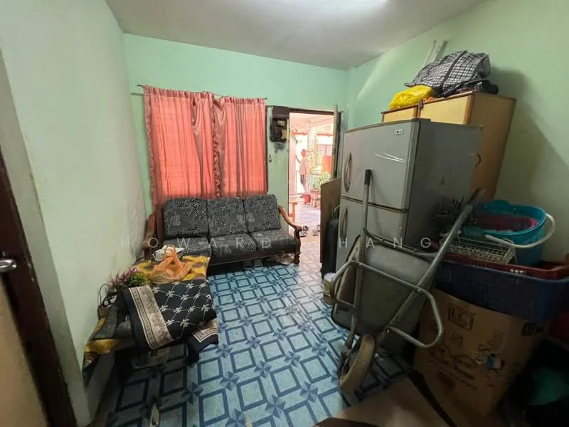 Living features: grey fabric 3-seater sofa, blue patterned tile flooring, green painted walls, orange curtains, refrigerator, wooden cabinet, wheelbarrow, storage boxes, decorative items on cabinet.